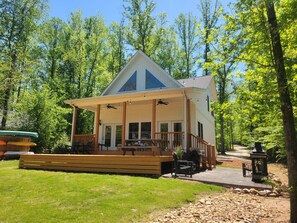 A cabin with a covered porch, a deck, and a patio area.