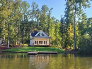 A house with a gabled roof, surrounded by a pond and trees.