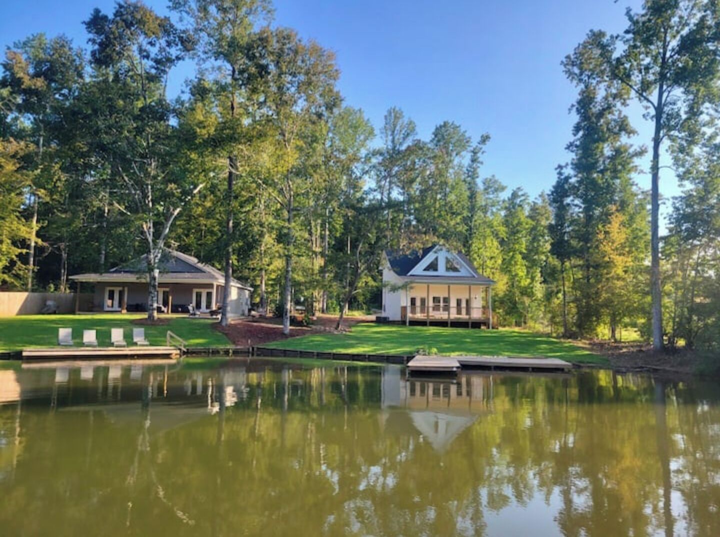 A lakeside property with two houses, a dock, and a grassy area with lounge chairs.