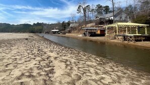 A riverside beach with a sandy shore, a wooden pier, and a building with a covered area. - Waverly Creek Retreat-kayaks/fire pit/pet friendly (Jackson's Gap)
