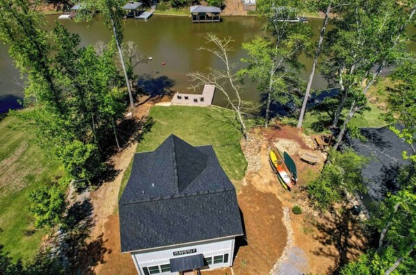 A house with a dark roof, surrounded by a grassy yard and a pond.
