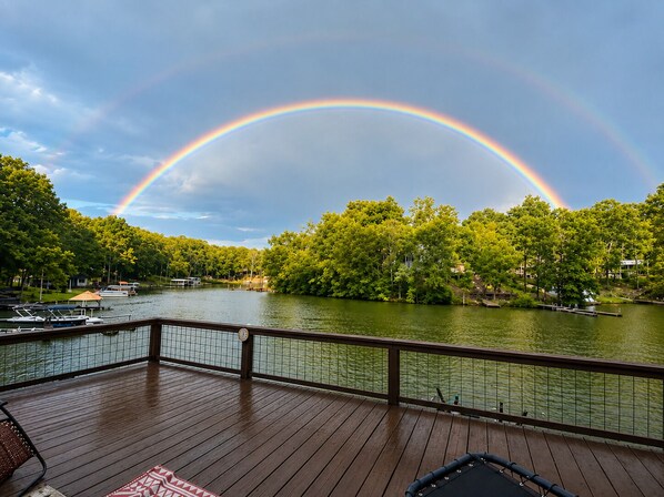 A deck with a view of a lake, boats, and a rainbow.