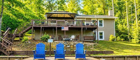 A lakeside property with a dock, outdoor seating, and a house with a covered patio.