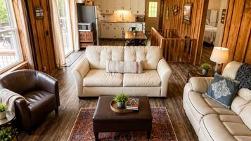 A spacious living room with a large ceiling fan, a fireplace, and a view of the kitchen.