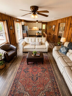 A spacious living room with a large ceiling fan, a fireplace, and a view of the kitchen.