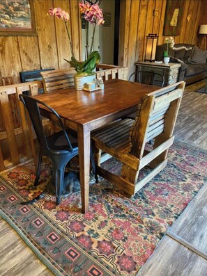 Una mesa de madera con sillas, un tapete estampado y una planta en maceta.