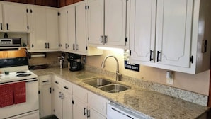 Una cocina con armarios blancos, encimera de granito, estufa, cafetera y lavaplatos.