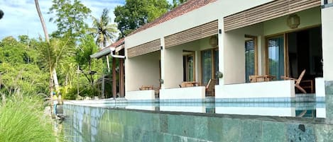 A modern resort with a swimming pool, wooden deck, and tropical vegetation.