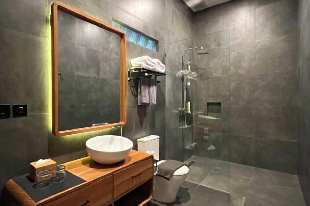A modern bathroom with a large mirror, a wooden vanity, a white sink, and a glass shower enclosure.