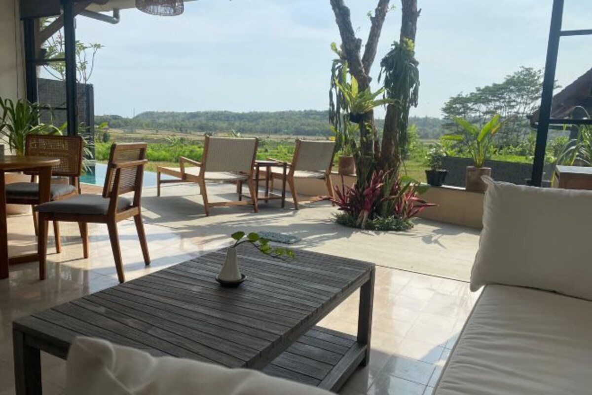 A spacious outdoor area with a wooden table, chairs, and a sofa. There are potted plants and a view of a lush landscape.