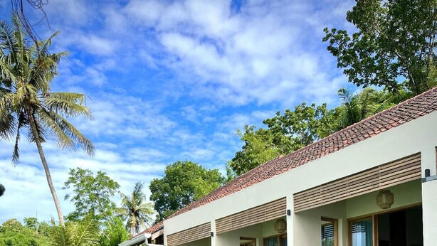 A modern resort with a swimming pool, wooden deck, and tropical vegetation.