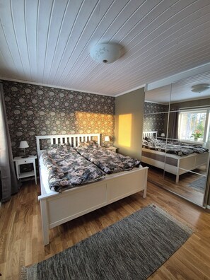 A bedroom with a bed, a nightstand, a lamp, a mirror, and a window.