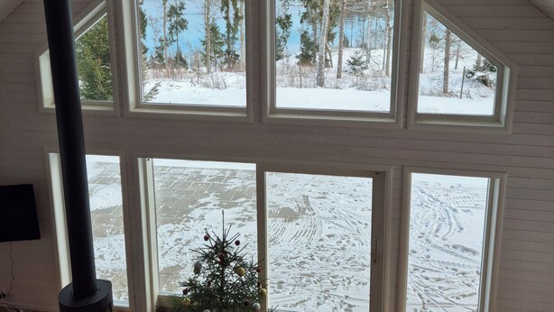 A high-ceilinged room with large windows, a wood-burning stove, and a small Christmas tree. - Berget Lövanäs 2, Newly built modern house in secluded location with own jetty and boat (Korsberga)