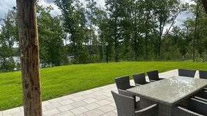 An outdoor patio with a table and chairs, surrounded by a grassy lawn and trees.