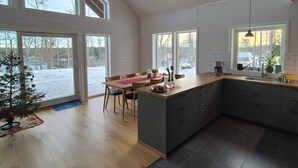 A spacious kitchen with a large island, wooden flooring, and large windows offering views of a snowy landscape. - Berget Lövanäs 2, Newly built modern house in secluded location with own jetty and boat (Korsberga)