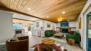 A spacious living area with a wooden ceiling, a fireplace, green sofas, and a kitchen in the background. - Newly Remodeled Mountainside Duplex w/ Epic Views-Upper Floors, Optional Hot Tub (Durango)