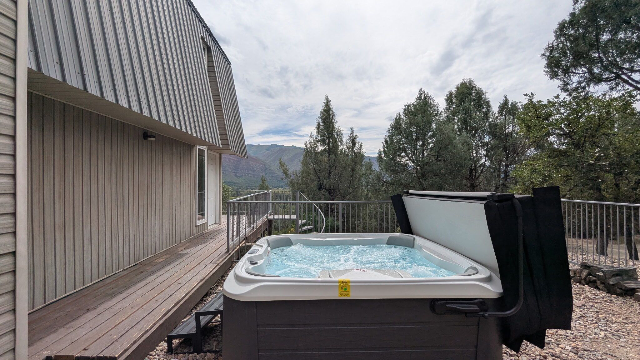 Una vasca idromassaggio su un pontile di legno con vista su montagne e alberi.