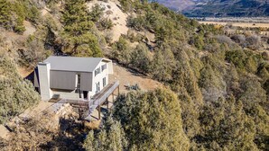 A modern two-story house with a flat roof, situated on a hillside surrounded by dense forest. - Newly Remodeled Mountainside Duplex w/ Epic Views-Upper Floors, Optional Hot Tub (Durango)