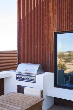 Un barbecue doté d’un écran numérique, une table en bois et une fenêtre donnant sur un paysage désertique.