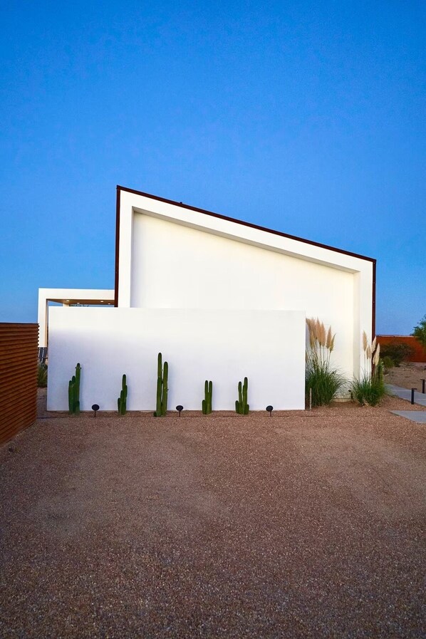 Un bâtiment moderne doté d’un toit plat et d’une façade blanche, entouré d’une allée gravillonnée et de cactus.