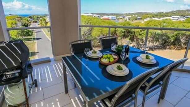 Ein Balkon mit einem Tisch für vier Personen, Gartenstühlen und Blick auf einen Weinberg und entfernte Gebäude.