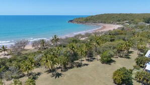 Vue aérienne d’une zone côtière avec une plage, des palmiers et un bâtiment équipé de panneaux solaires.