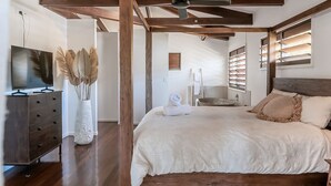 Une chambre à coucher avec un grand lit, des poutres en bois, une télévision, une commode et un vase contenant des plantes séchées.