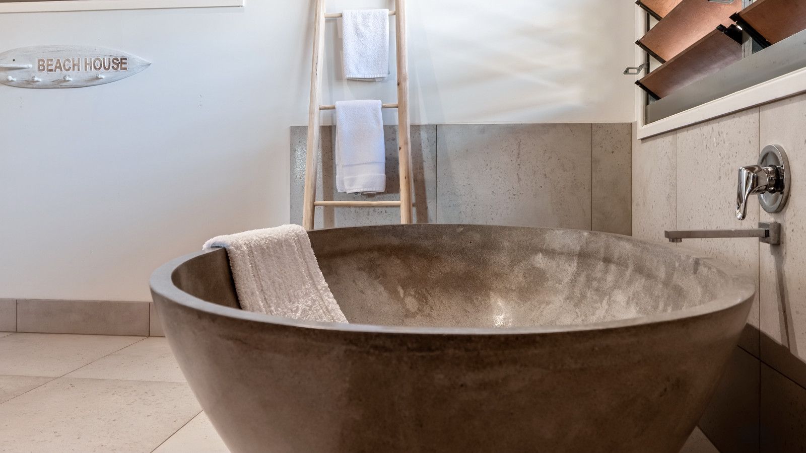 Eine große, runde, metallische Badewanne mit einem Handtuch darin, eine Holzleiter und ein Handtuchhalter an der Wand.