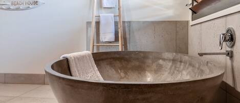 Eine große, runde, metallische Badewanne mit einem Handtuch darin, eine Holzleiter und ein Handtuchhalter an der Wand.