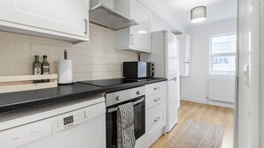 A modern kitchen with white cabinetry, a Bosch dishwasher, a microwave, and a window providing natural light.