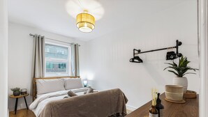 A bedroom with a bed, bedside table, lamp, and a view of a building through the window.