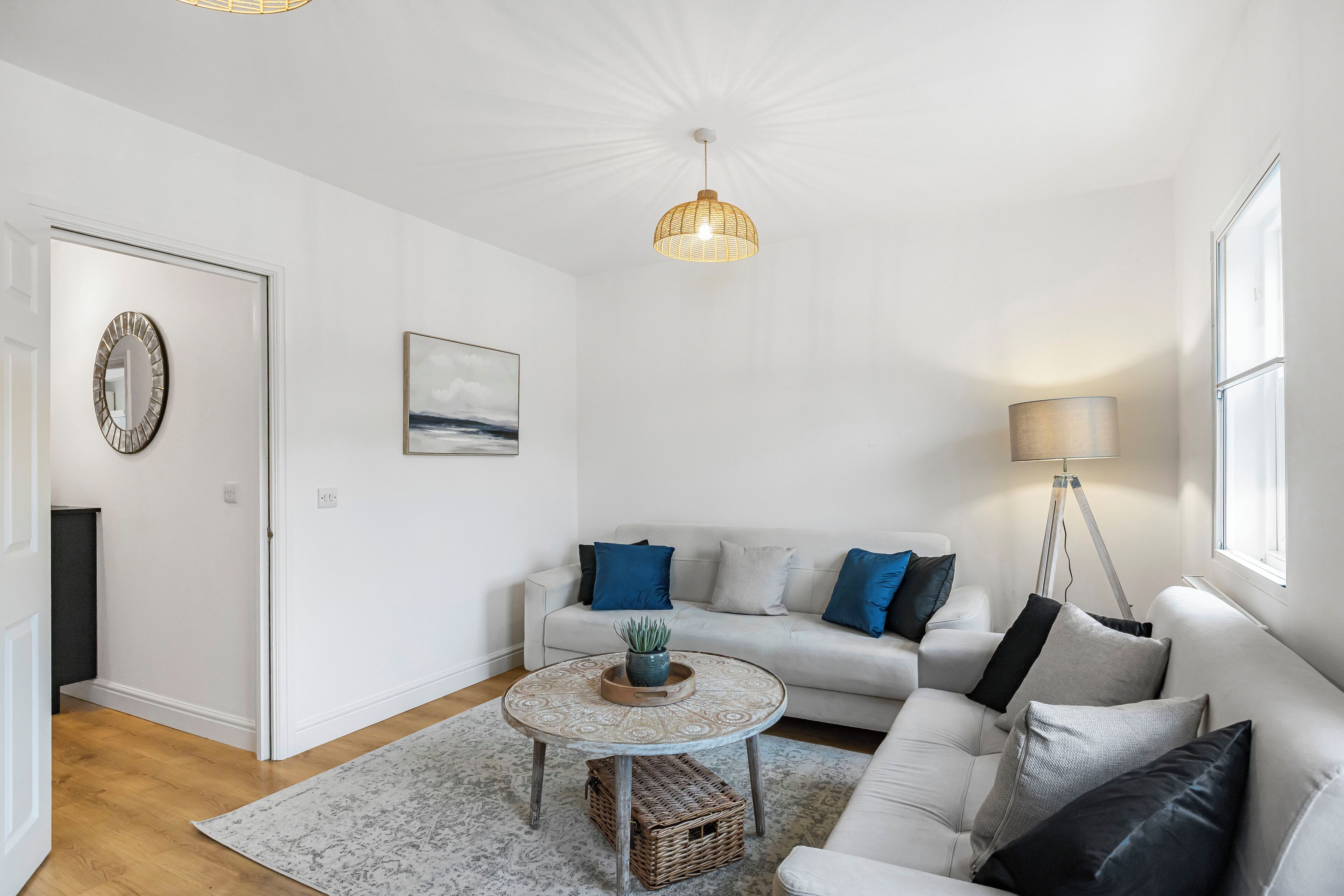 Ein modernes Wohnzimmer mit einem weißen Sofa, einem runden Couchtisch mit einer Pflanze, einer Stehlampe und einer Deckenleuchte.