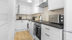 A modern kitchen with white cabinets, a washing machine, an oven, and a microwave.