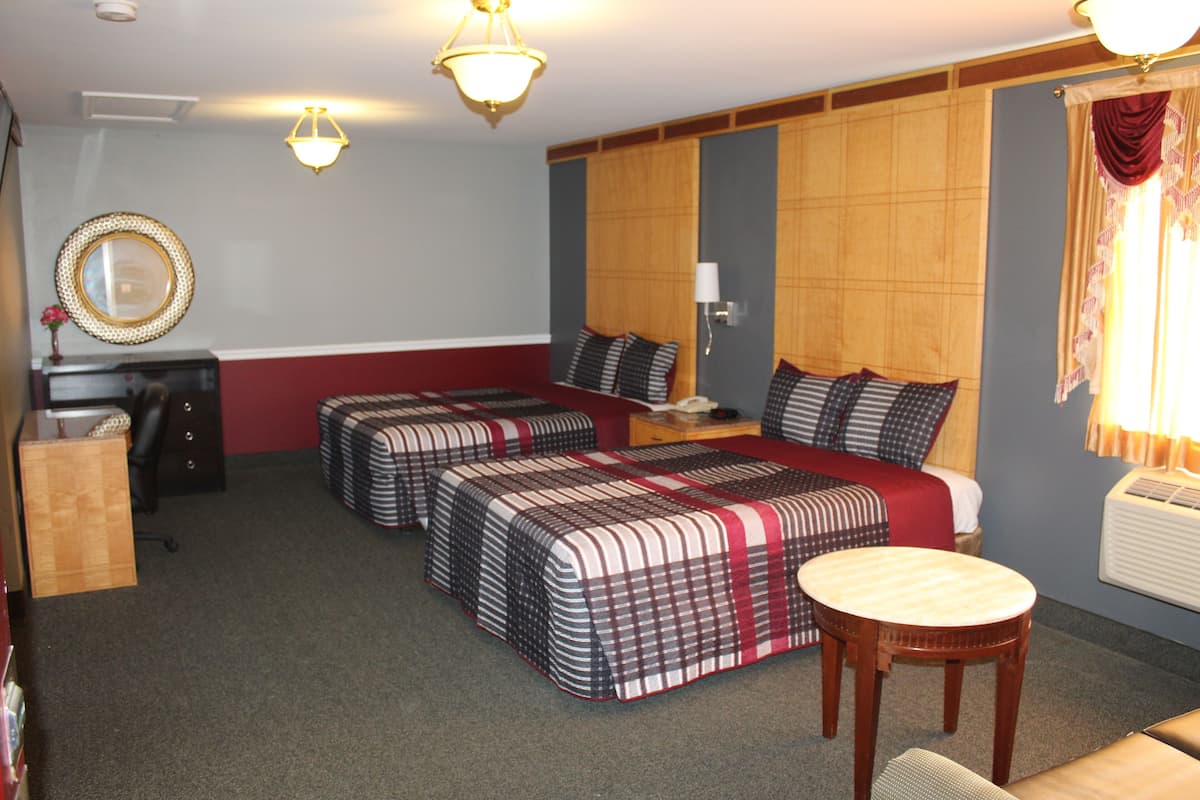 A hotel room with two beds, a desk, a chair, a lamp, and a mirror.