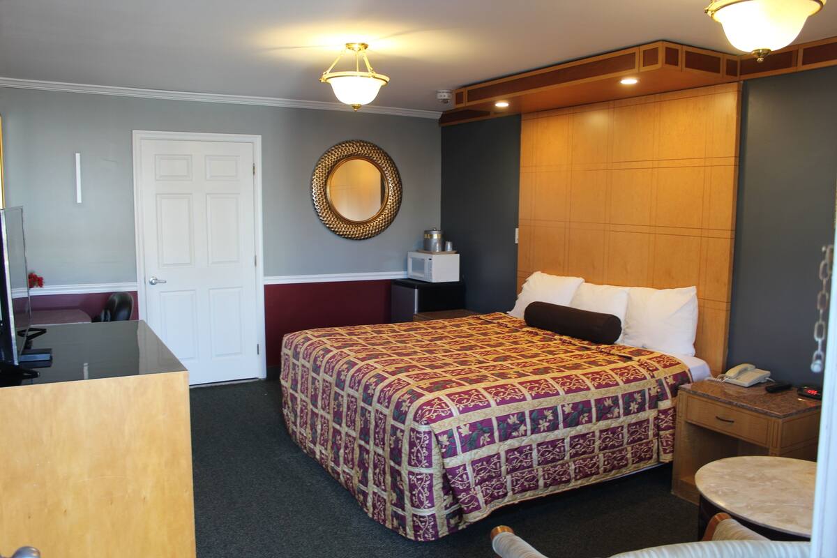 A hotel room with a large bed, a desk, a chair, a bedside table, a lamp, and a mirror on the wall.