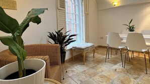 A dining area with a high arched window, a wicker chair, a cushioned chair, and a dining table with chairs. - Stylish Georgian Townhouse in Rye Citadel (Rye)