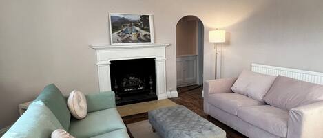 Una sala de estar con chimenea, dos sofás, un tapete y una araña.