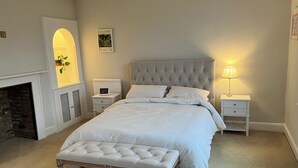 A neatly arranged bedroom with a large bed, a bedside table with a lamp, a small bedside table with a picture, and a bench in front of the bed. - Stylish Georgian Townhouse in Rye Citadel (Rye)