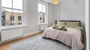 A bedroom with a large window, a bed with a beige bedspread, and a patterned rug. - Modern 2 Bedroom Townhouse Flat in King's Cross (London)