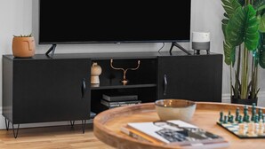 A modern living room with a flat-screen TV, a black entertainment unit, a coffee table with books and a chess set, and a large green plant. - Modern 2 Bedroom Townhouse Flat in King's Cross (London)