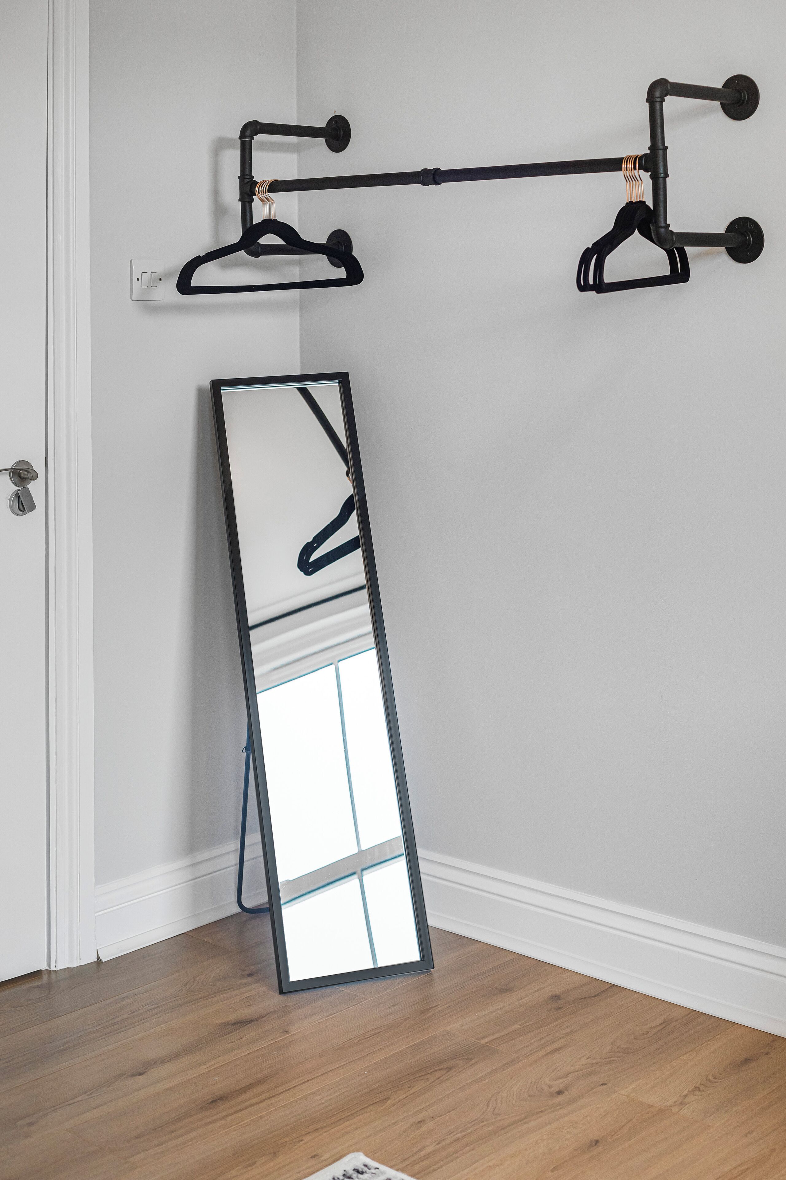 A mirror leaning against a wall with a black metal rack above it.