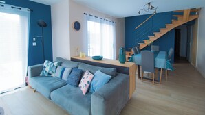 A modern living room with a grey sofa, a wooden dining table, and a staircase leading to another level. - Contemporary family home with outdoor pool and garden (Prinquiau)