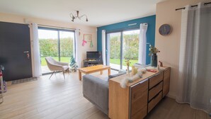 A modern living room with a sofa, a wooden coffee table, and a TV. There is a sliding glass door leading to a balcony. - Contemporary family home with outdoor pool and garden (Prinquiau)