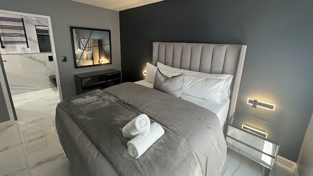 Een moderne slaapkamer met een groot bed, een nachtkastje, een spiegel en een wandlamp.
