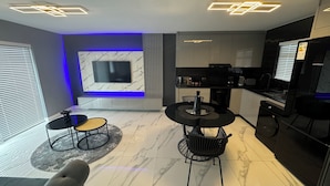 Een moderne woonkamer met een televisie, zitplaatsen en een keukenhoek.