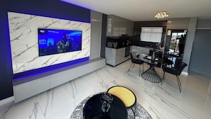 Een moderne keuken met een inbouwmagnetron, een eethoek met zwarte stoelen en een televisie bevestigd aan een marmeren muur.