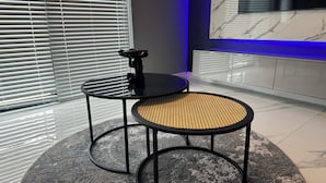Een moderne kamer met twee ronde tafels, waarvan één een zwart oppervlak heeft en de andere een geweven zitting, plus een marmeren wand met een televisie.