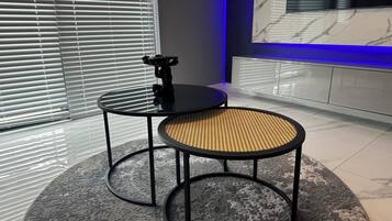 A modern room with two round tables, one with a black surface and the other with a woven seat, and a marble wall with a TV.