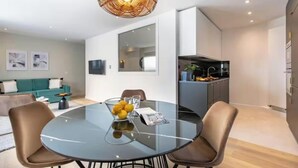 A modern living room with a glass dining table, a sofa, and a kitchen area.