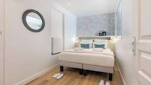 A modern bedroom with a bed, a round mirror, a radiator, and a view of the city through a window.